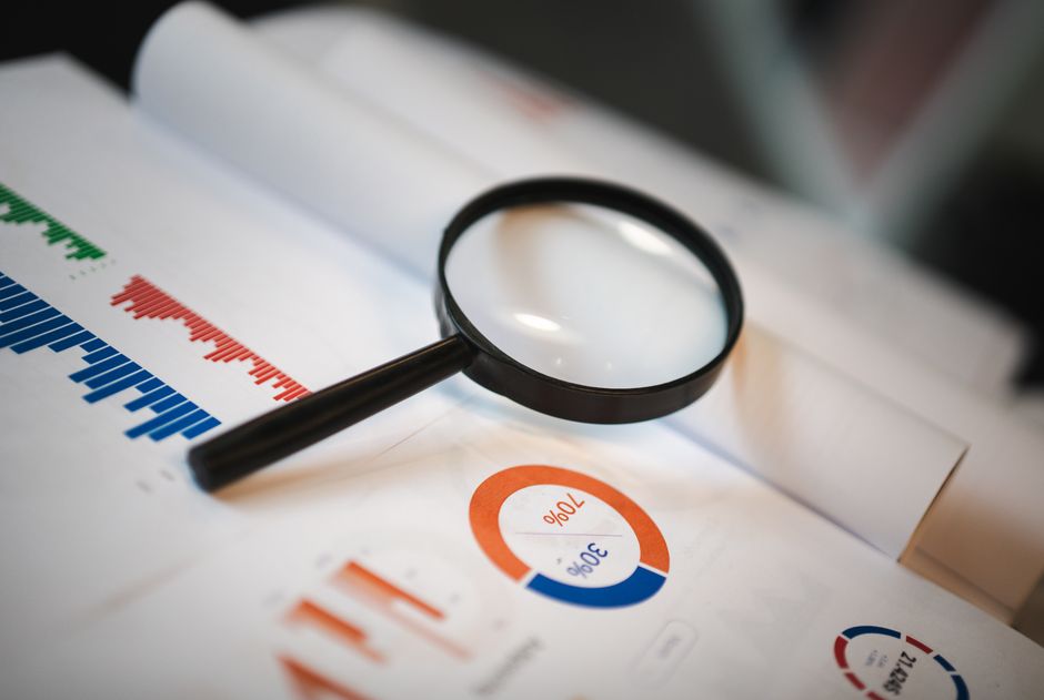 A close-up shot of a hand holding a magnifying glass over a detailed architectural blueprint, symbolizing the in-depth analysis of a real estate franchise model.