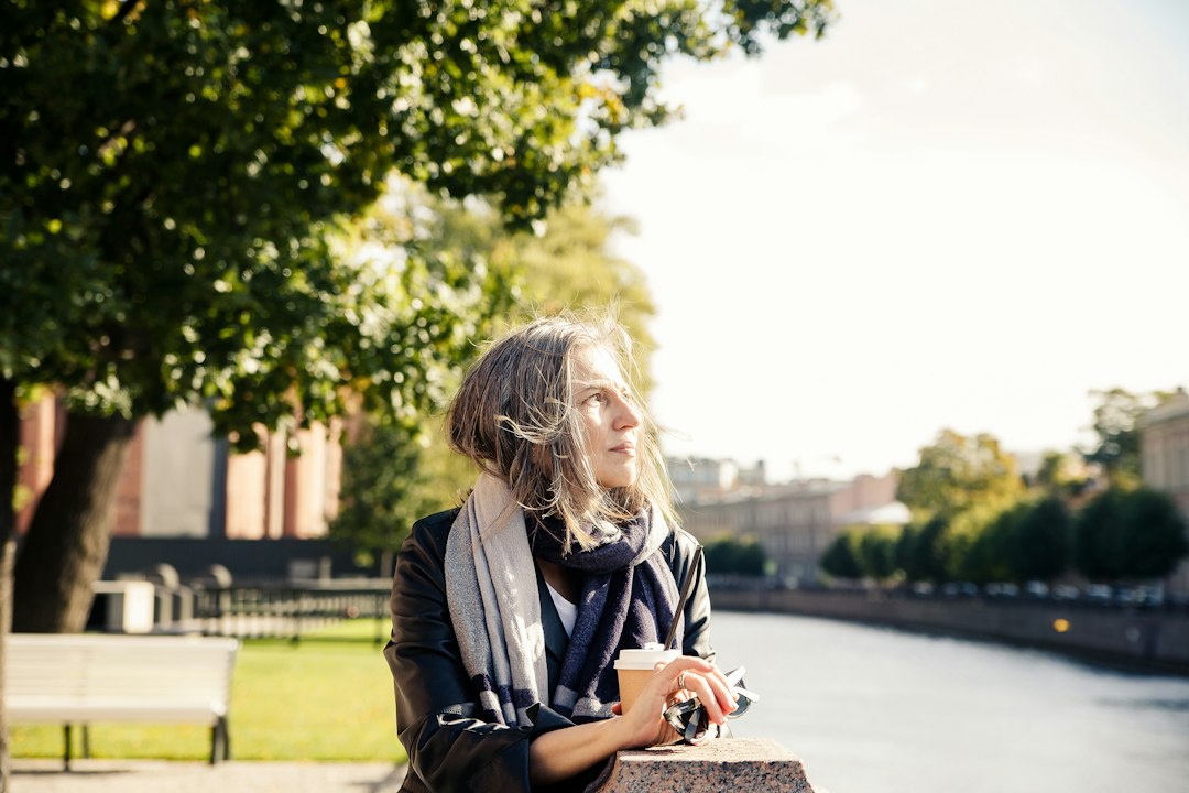 A woman finds a moment of peace, sipping tea while sitting calmly in a room filled with packed moving boxes, symbolizing self-care during a stressful home sale.